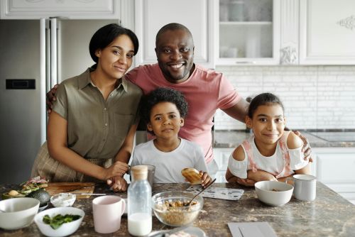 A joyful family of four smiling together at the kitchen counter during breakfast time.